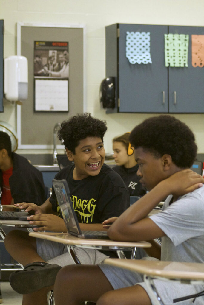 A boy smiles when exploring electronic beat making on his computer, next to his peers