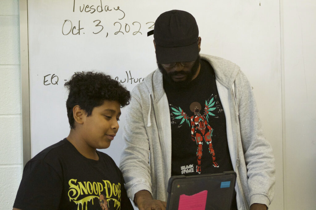 A Black instructor helps a student with electronic beat making on the computer