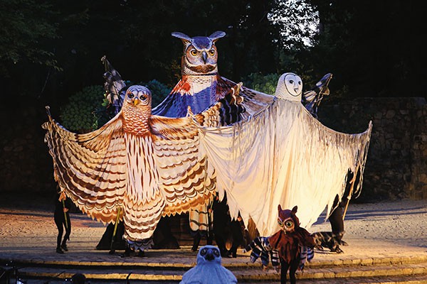three giant owl puppets being operated by a group of puppeteers in black.