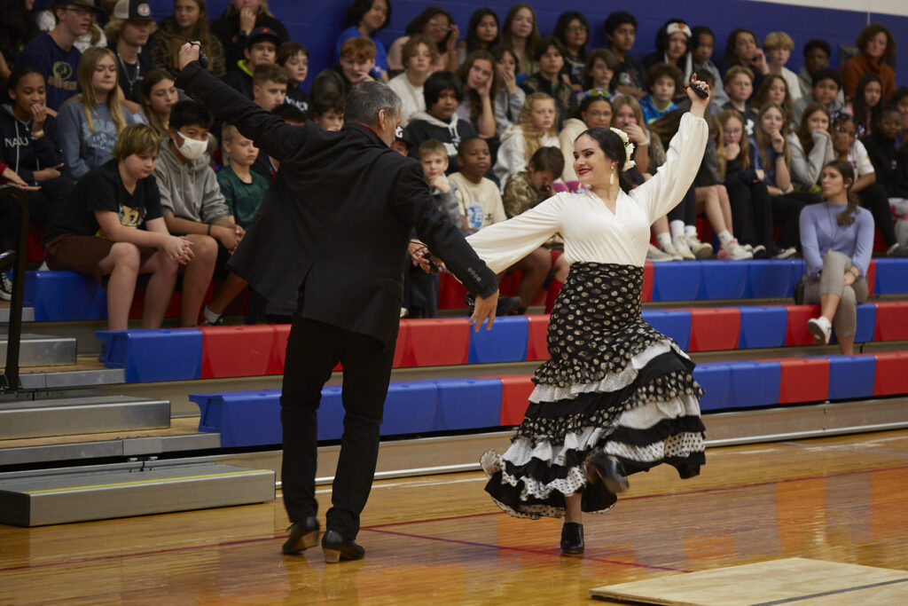 Flamenco dancers perform in a school gym in front of an audience of students. 