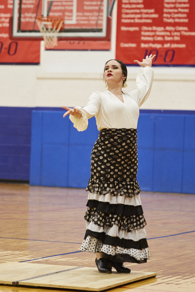 Flamenco dancers perform in a school gym in front of an audience of students. 