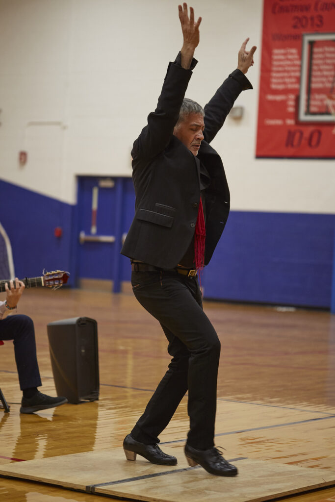 Flamenco dancers perform in a school gym in front of an audience of students.