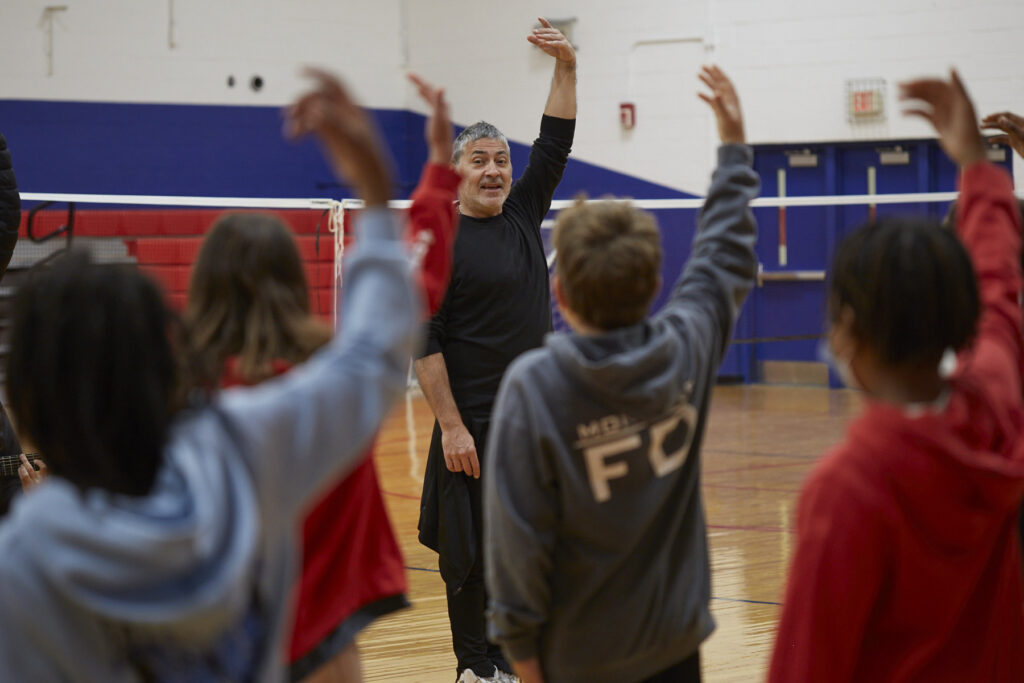 Flamenco dancers work with students to learn choreography in a school gym.