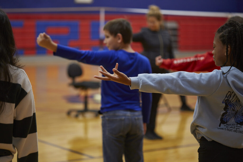 Flamenco dancers work with students to learn choreography in a school gym.