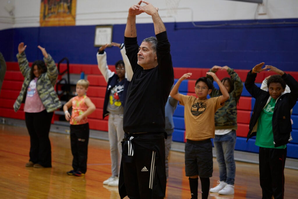 Flamenco dancers work with students to learn choreography in a school gym.