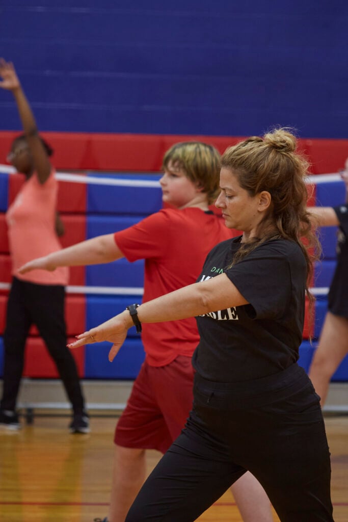 Flamenco dancers work with students to learn choreography in a school gym.