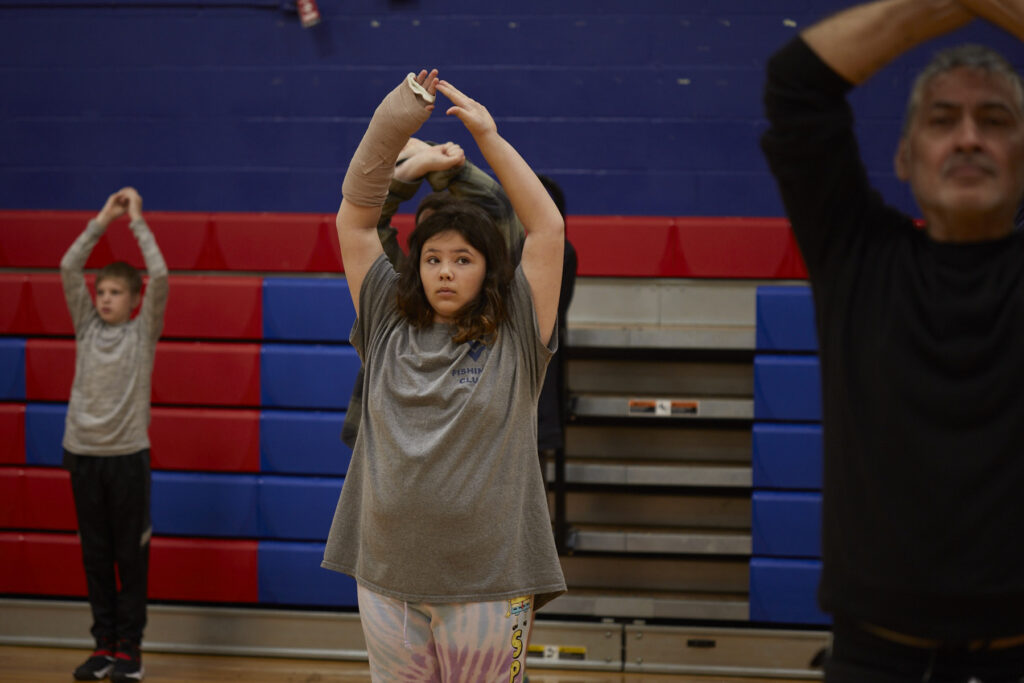 Flamenco dancers work with students to learn choreography in a school gym.