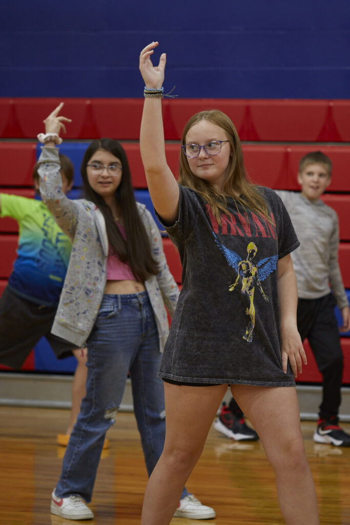 Flamenco dancers work with students to learn choreography in a school gym.