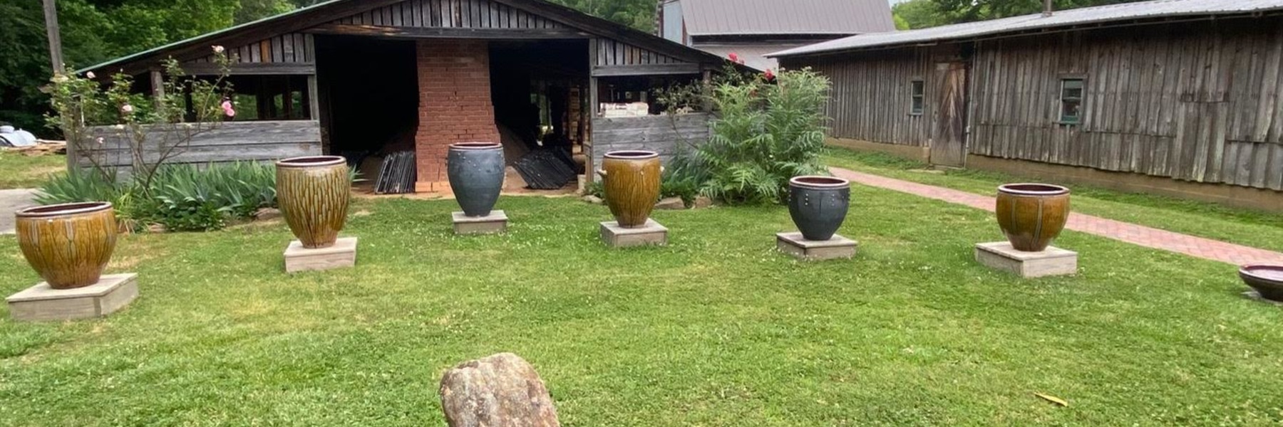 a display of large ceramic pots lined up on a lawn in front of a studio building