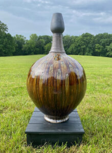 a large brown vase displayed on a small table on a lawn