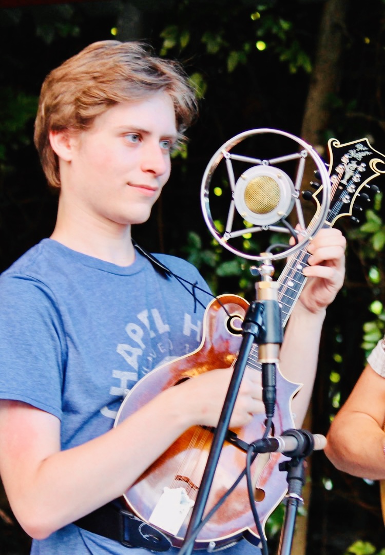 a young man in a blue t-shirt playing mandolin in front of a microphone and stand