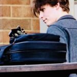 a young man is sitting at a picnic table with his back turned playing the mandolin
