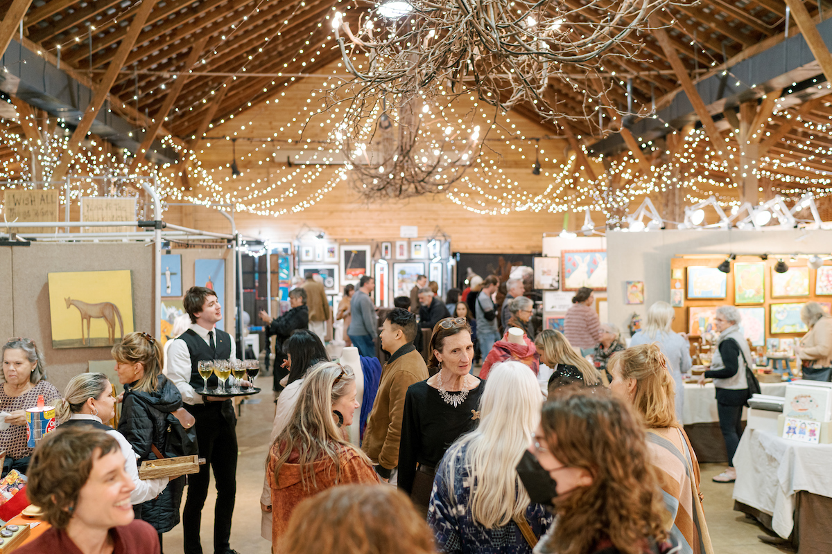 a wide view of a gallery event. champagne is being served while collectors mingle under string lights.