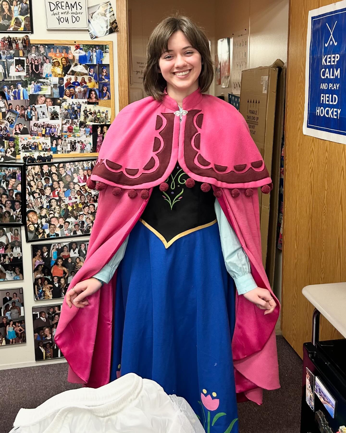 a teenage girl in costume of Princess Anna from Disney's Frozen. Black and blue dress with pink cape.
