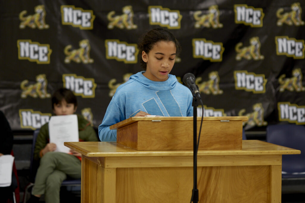 A student reads aloud at a podium. 