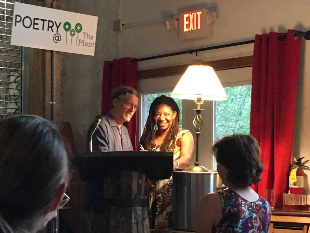 Photo of white man in glasses and a black woman with long hair standing behind a podium