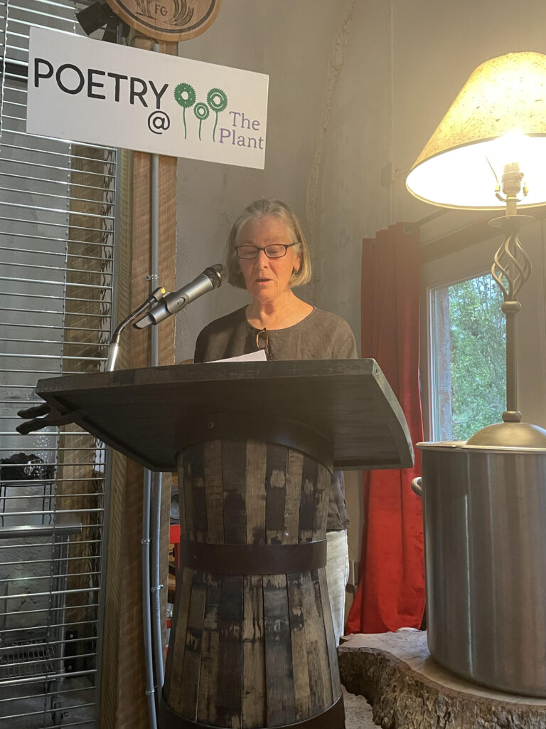 Photo of white woman with white hair and glasses standing behind a podium 