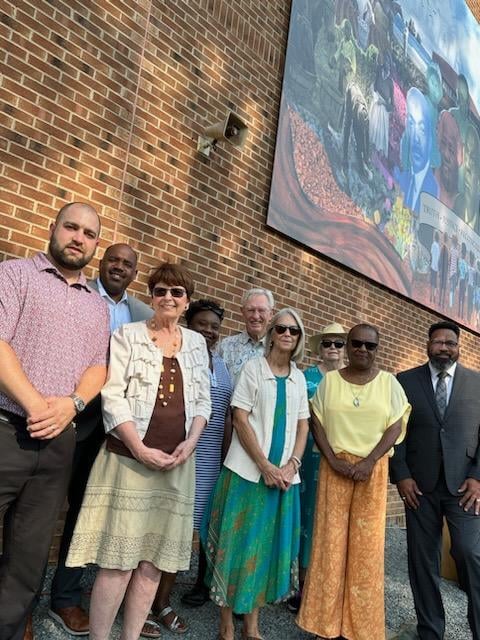 A group of nine people standing in front of a mural and brick wall