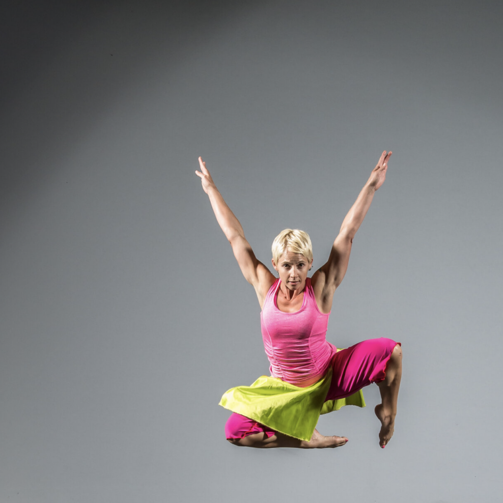 Photo of blonde female dancer leaping in air with arms over her head