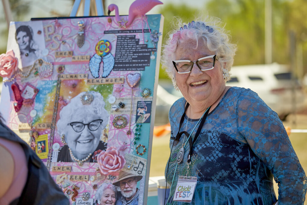 Chatham legend Pam Smith smiles beside the mixed media art she inspired JumpstART artist Tanja Lipinski Cole to create. The canvas is full of bright colors and textures.