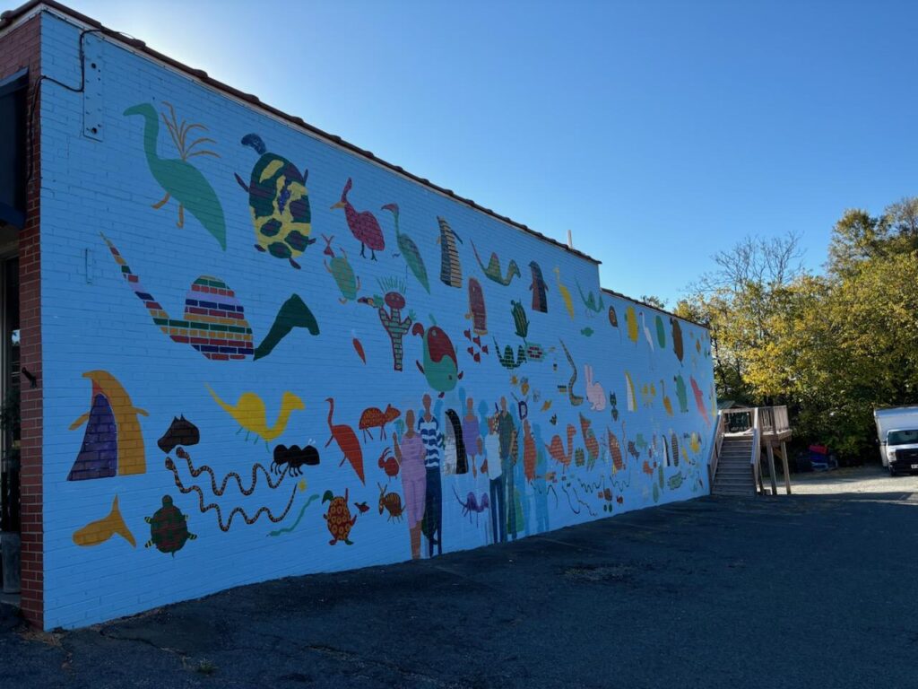 Mural of turtles, snakes, and other critters on a blue background on the side of a brick building.