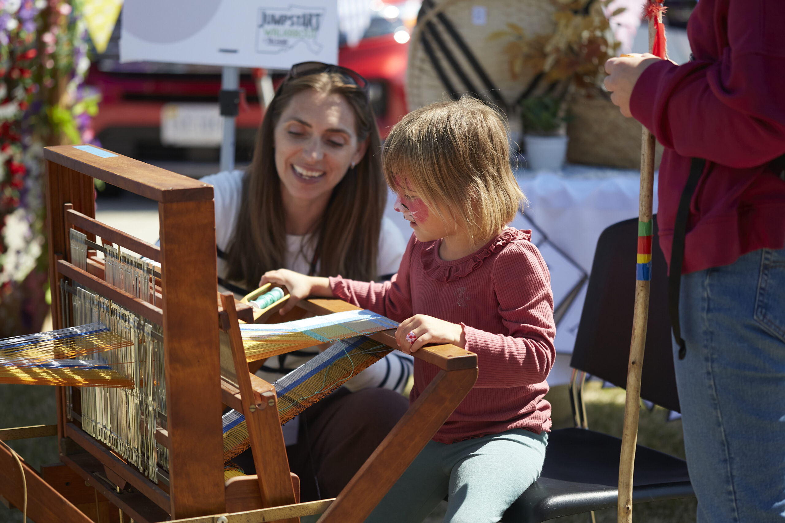 a woman helping a child on a weaving loom