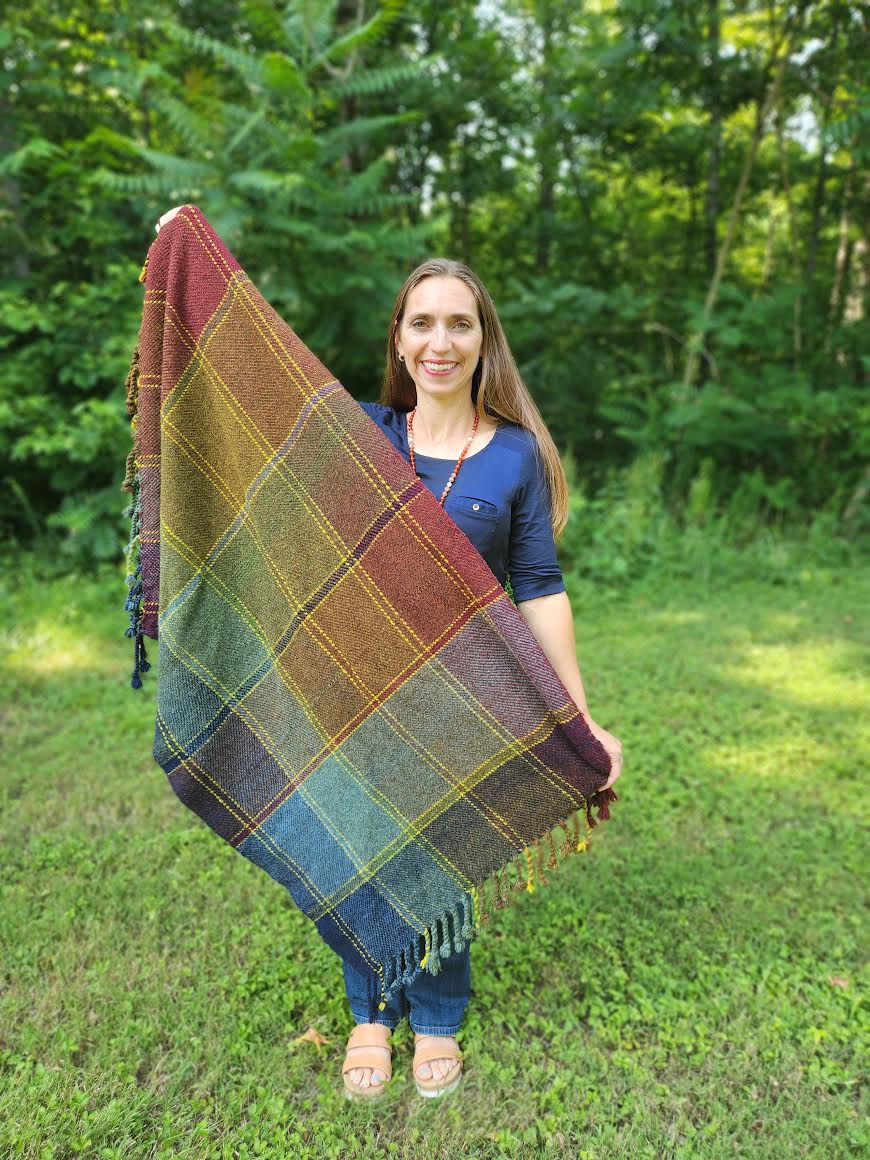 a woman smiling displaying a shawl she has made