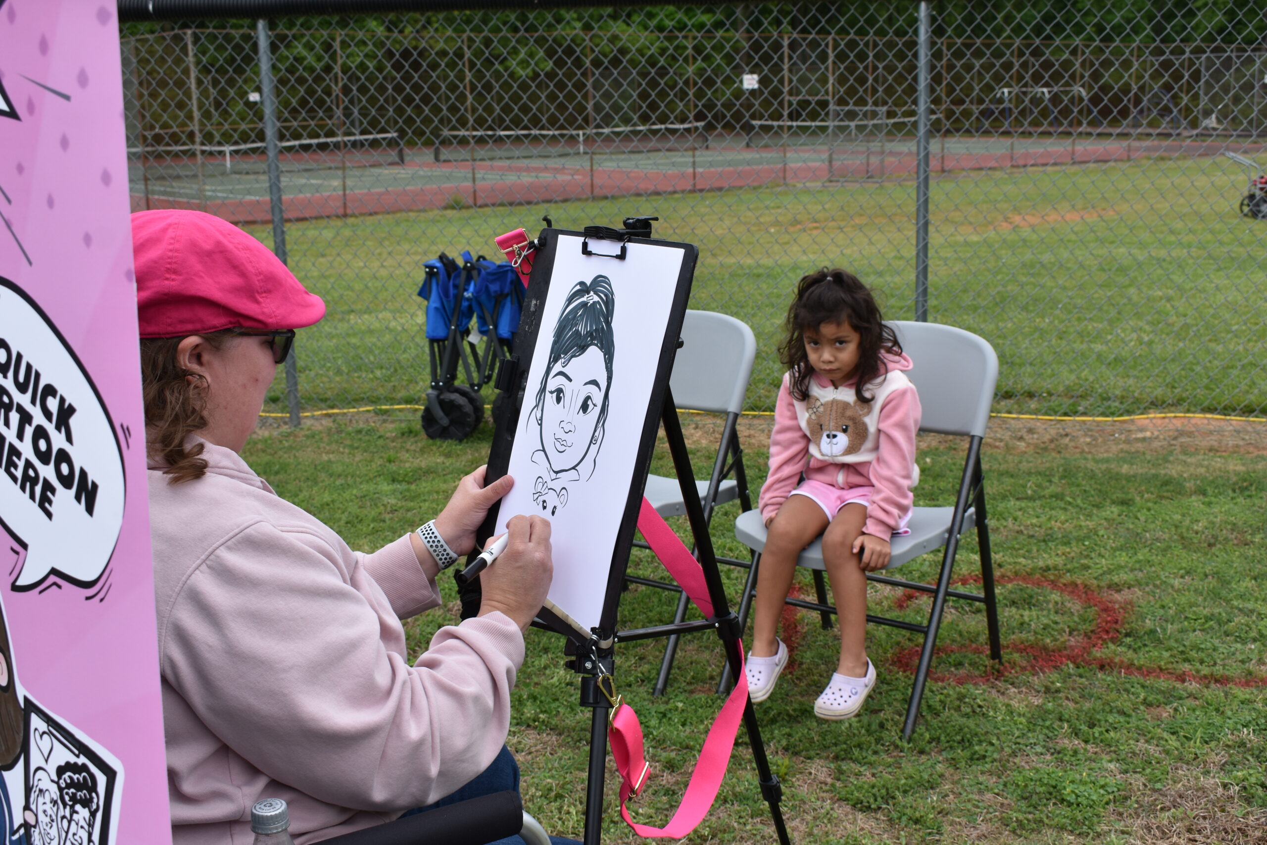 a caricature artist in a pink hat drawing a little girl