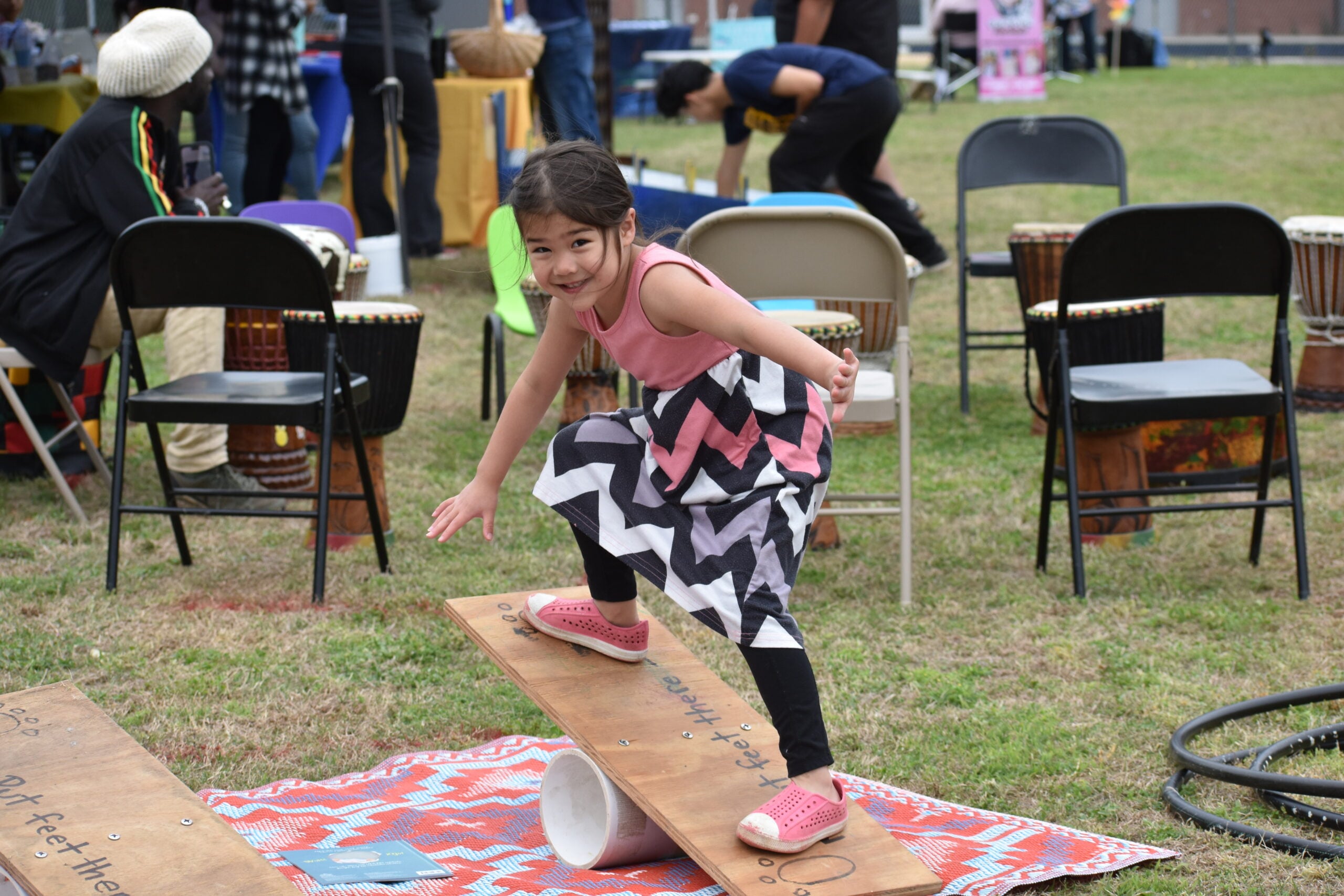 a girl in a vibrant patterned dress balanced on a board like a skateboard.