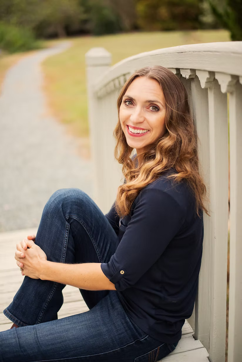 a woman with long brown hair sitting with her back against a railing leading to a gravel path