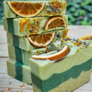 A stack of green soap bars, full of dried citrus slices, herbs, and flowers.