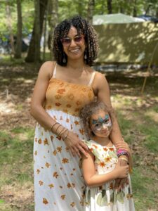 Sunny outdoor photo of a smiling Black woman and young girl leaning against her. They both wear flower patterned dresses.