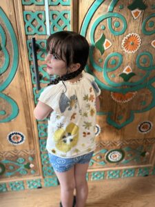 Young girl smiling, wearing a white shirt with colorful herbal and botanical prints.