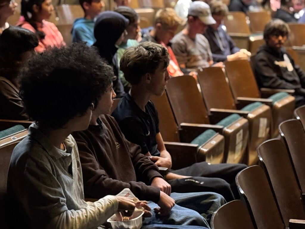 Teenagers in a school auditorium, watching the stage closely.