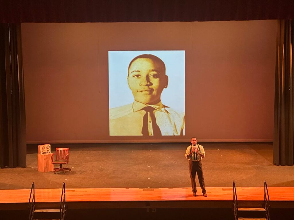 Black actor onstage in front of large projection of young Emmett Till.