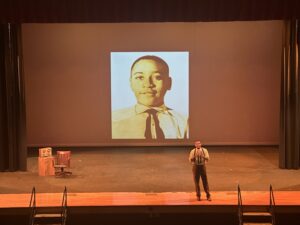 Black actor onstage in front of large projection of young Emmett Till.