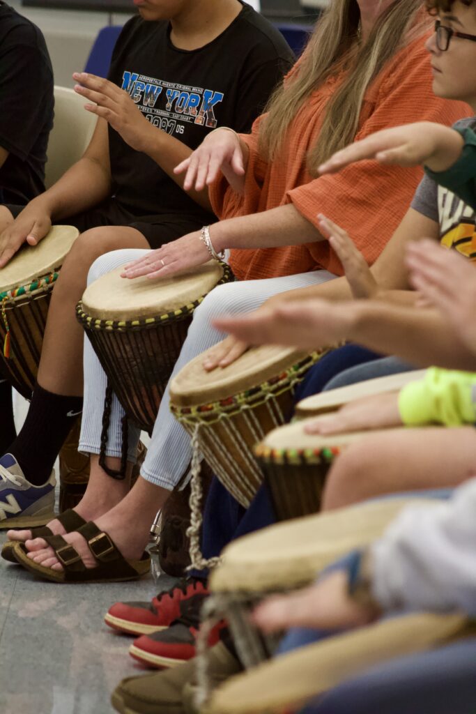 Students hands are seen playing djembe drums.