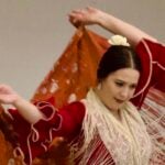 Flamenco dancer performs in red dress, with red shawl, as students watch.