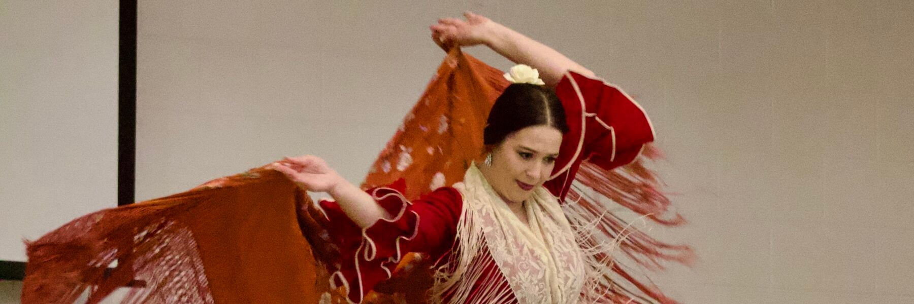 Flamenco dancer performs in red dress, with red shawl, as students watch.