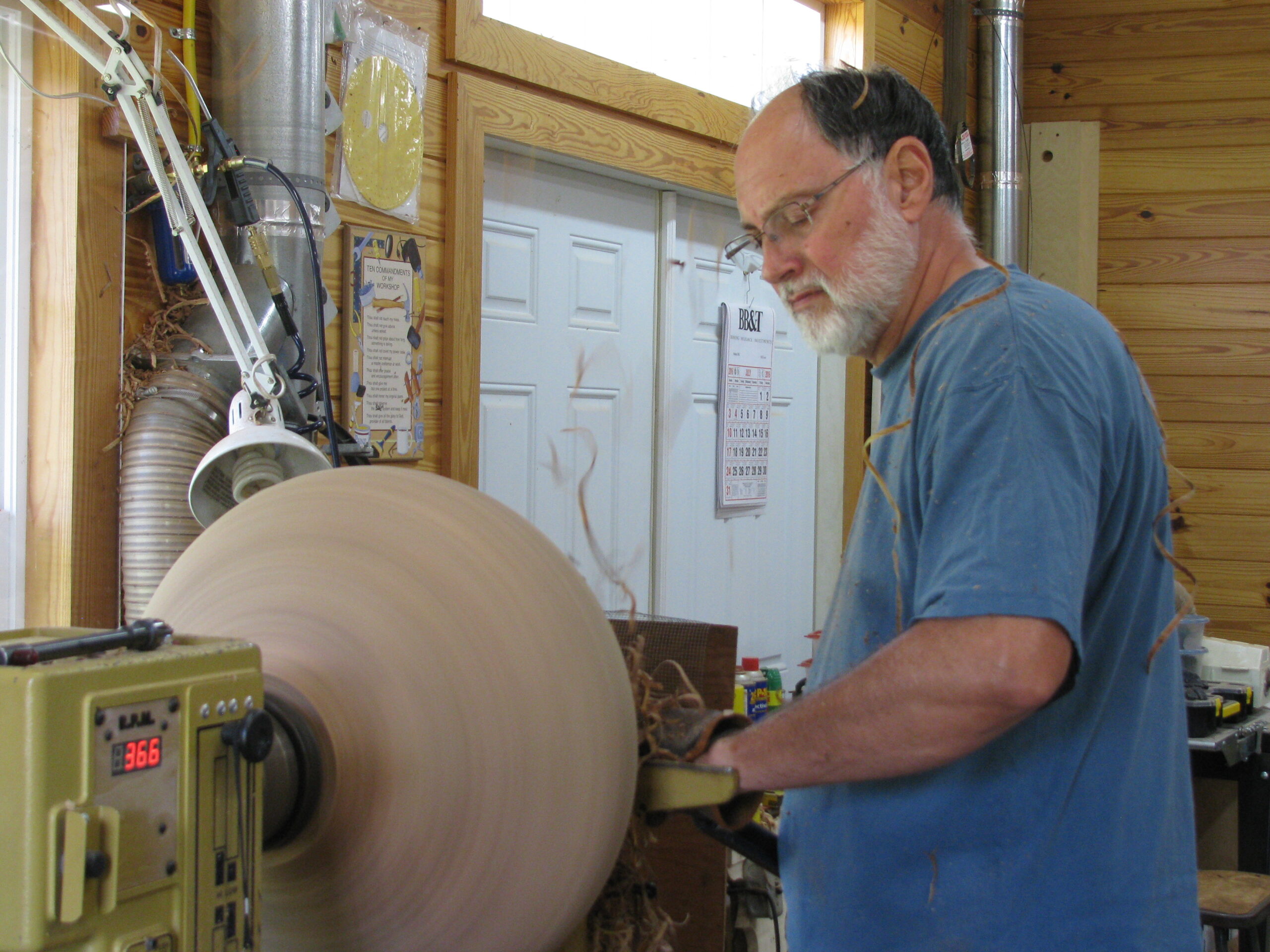 a man with short grey beard and glasses is turning wood.