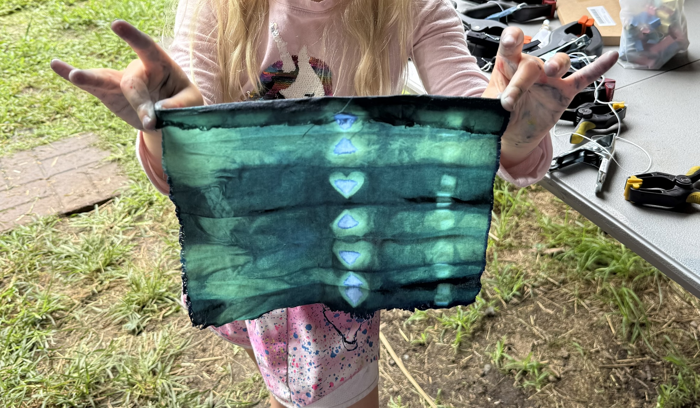 Young girl holding up green and blue indigo dyed fabric swatch with hearts down the center