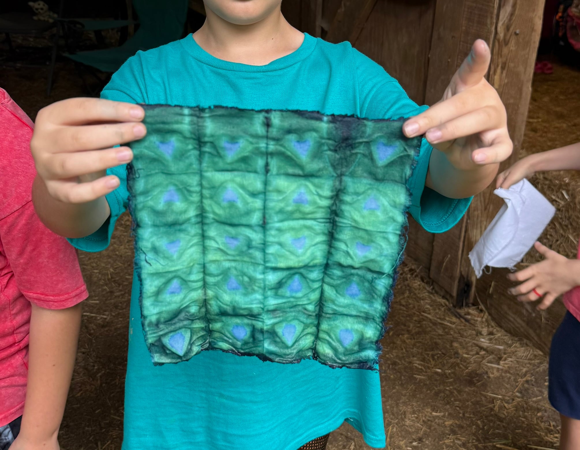 Young boy holding up greenish blue indigo dyed fabric with squares and hearts