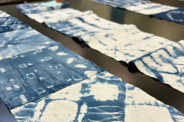 Rows of white fabric squares with indigo tie-dye patterns are laid out on a dark table.