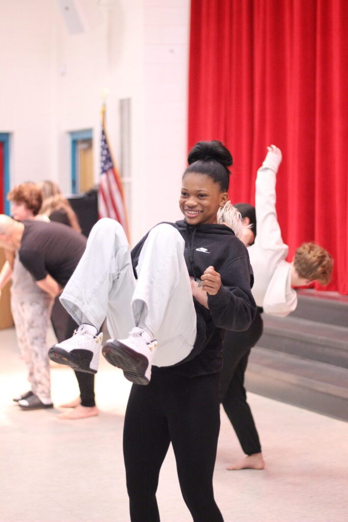 Smiling young black girl being lifted in the air, knees bent, by a Black Box dancer
