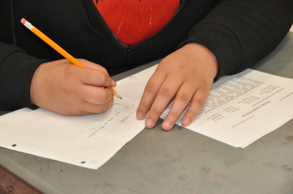 A close-up shot of hands writing on paper with a pencil.