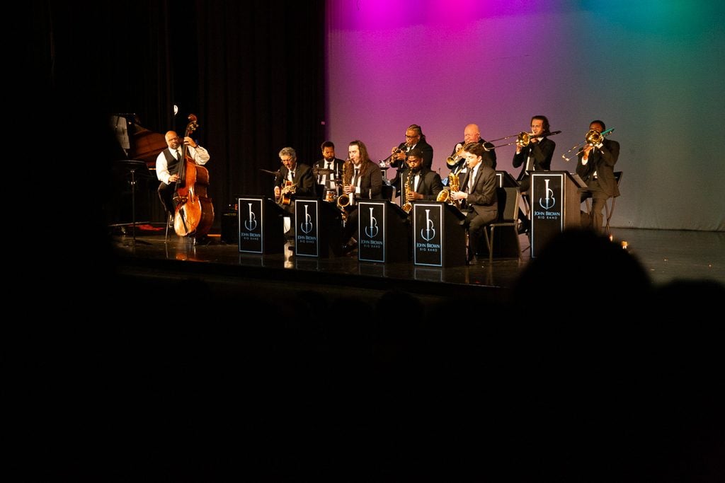 John Brown's little big band playing on stage with a pink and teal background.