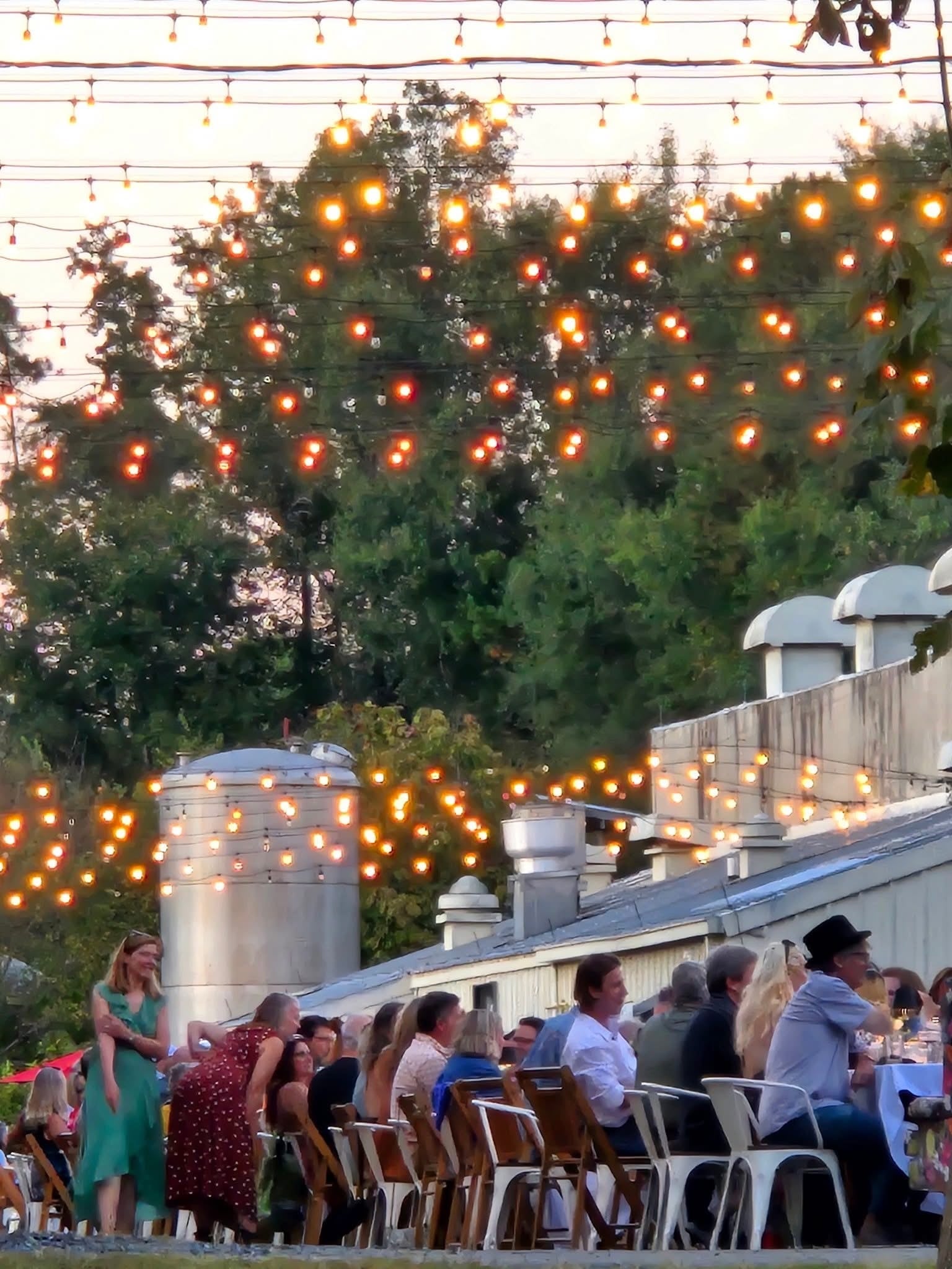 A long banquet table laid out under string lights outside on a temperate evening.